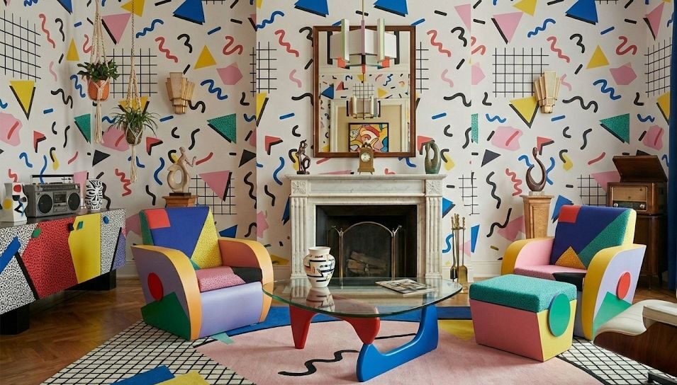 Salotto in stile anni ’80 dal design Memphis con colori vivaci, forme geometriche e arredi eccentrici multicolor. La carta da parati grafica, le poltrone dalle linee astratte, il tavolino scultoreo e i dettagli pop creano un’atmosfera dinamica, creativa e giocosa tipica dell’estetica postmoderna dell’epoca