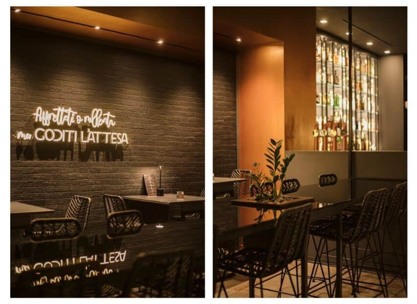 immagini di un progetto interior desisn horeca del uemè di Lecce, Immagine a sinistra: Interno del ristorante dall’atmosfera intima, con parete in mattoni scuri illuminata da faretti a soffitto. Una scritta luminosa decorativa crea un punto focale sulla parete. I tavoli sono essenziali, con piano chiaro e sedute nere intrecciate, mentre la luce calda contribuisce a rendere lo spazio accogliente ed elegante. Immagine a destra: Area dining con tavoli alti e sgabelli, caratterizzata da tonalità calde e avvolgenti. Sullo sfondo, una parete con bottiglie esposte e retroilluminate aggiunge profondità e interesse visivo. Un setto in finitura terracotta separa gli ambienti, mentre piccoli elementi verdi sui tavoli donano un tocco naturale e raffinato.