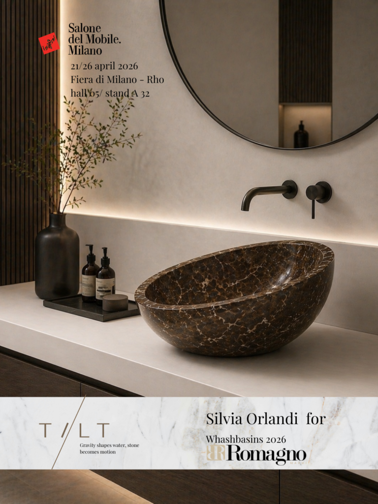 Locandina Salone del Mobile Milano 2026 con lavabo scultoreo in marmo scuro venato su piano chiaro, rubinetteria a parete nera, specchio rotondo e dettagli minimal, progetto “TILT” firmato Silvia Orlandi per Romagno.