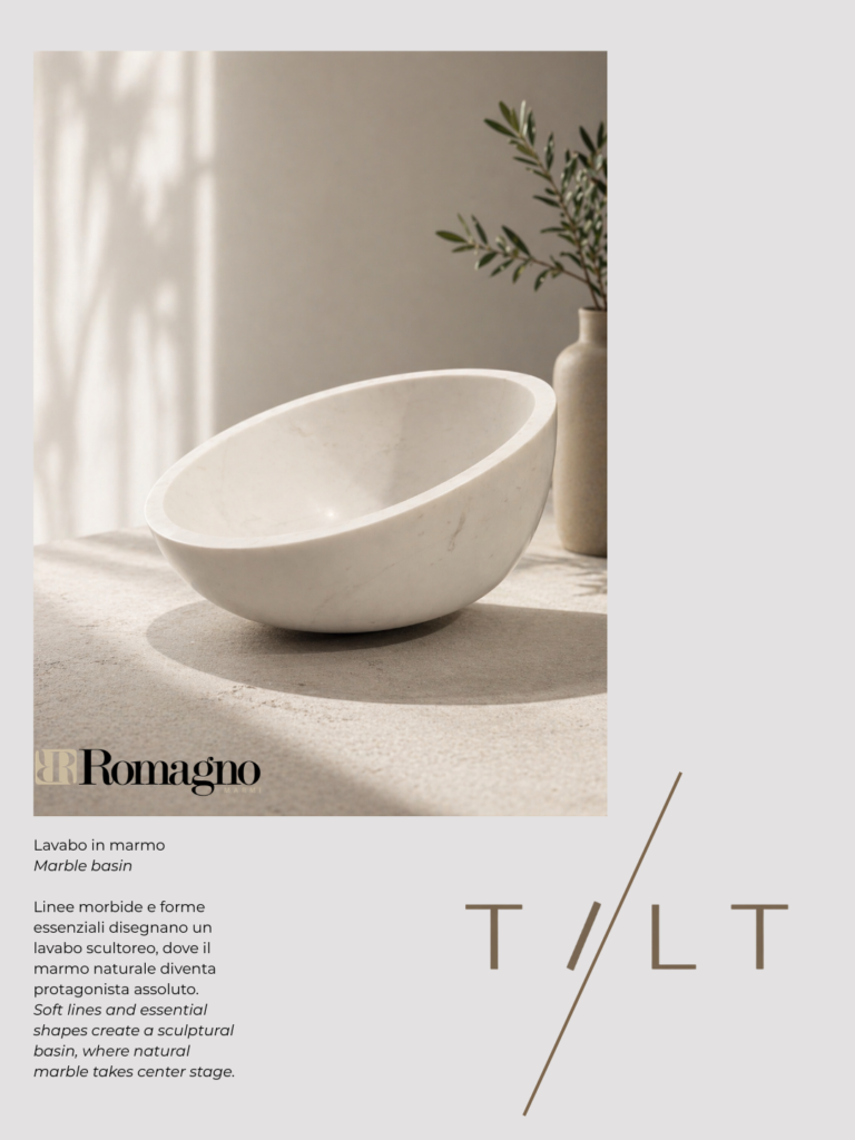 Lavabo scultoreo in marmo bianco dalle forme morbide e inclinate, appoggiato su piano chiaro in ambiente minimal luminoso, con testo descrittivo “TILT” e branding Romagno.