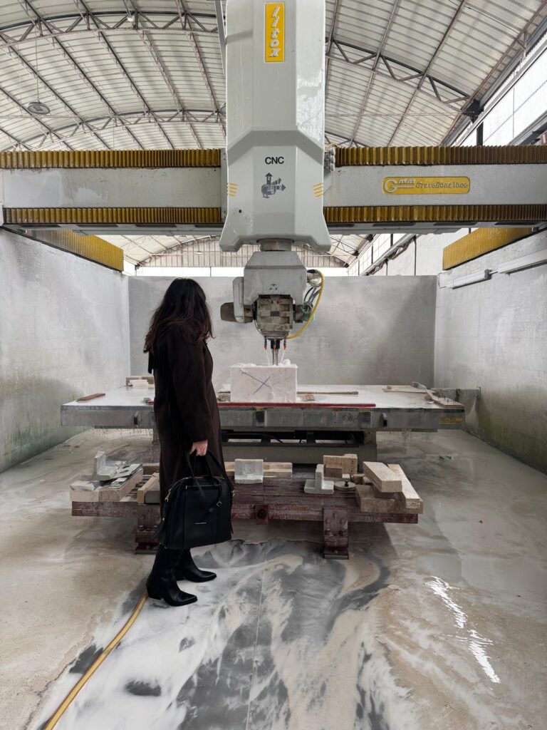 Silvia Orlandi osserva il lavabo Tilt grezzo scolpito da una macchina CNC in laboratorio, tra superfici bagnate e materiali grezzi in fase di lavorazione.